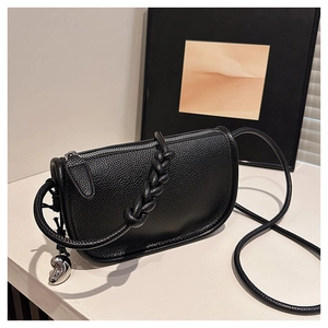 Détail d'un sac selle en cuir grainé noir avec bandoulière tressée et breloque cœur