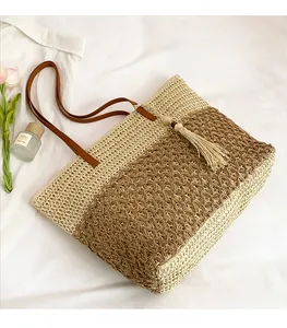 Detail of woven straw tote bag with brown leather handles and decorative tassel ornament