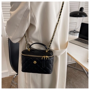 Detalle de bolso cubo acolchado negro con flor de camelia dorada y correa de cadena