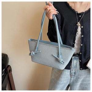 Détail du sac cabas bleu clair texturé avec nœuds décoratifs et fermeture éclair