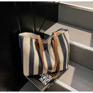 Detail of woven beach tote featuring blue stripes and brown leather handles on books