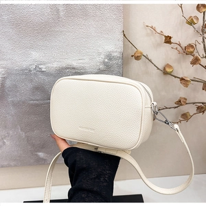 Dettaglio della pelle a grana litchi bianco crema su una borsa a tracolla minimalista
