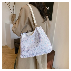 Detail of iridescent sequins on a white tote bag with gold ring hardware and leather strap