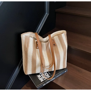 Close-up of woven straw tote bag with vertical stripes and leather straps on wooden stairs
