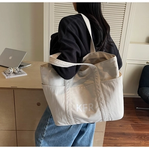 Detail of a beige canvas tote bag with KFR logo worn over the shoulder in an office setting