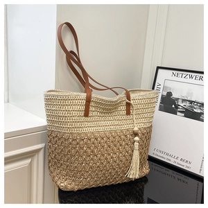 Detail of hand-woven straw tote bag with brown leather handles and decorative tassel