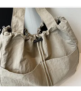 Detail of beige nylon drawstring tote bag featuring large functional front pockets