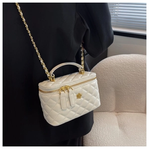 Detalle de bolso tipo cubo blanco acolchado con emblema floral dorado en una modelo