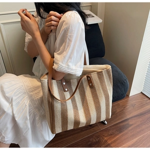 Detail of handwoven straw tote with brown leather straps and vertical stripes