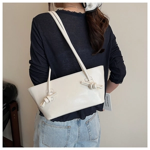 Détail d'un sac à bandoulière blanc minimaliste avec nœud décoratif sur la sangle