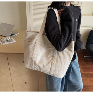 Detail of a beige oversized canvas tote bag with front pockets and KFR logo print