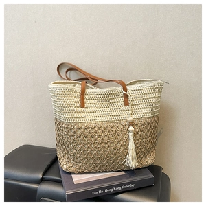 Detail of hand-woven straw tote with leather straps and white cotton tassel charm
