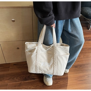 Detail of cream canvas tote bag showing KFR lettering, stitching, and side pockets