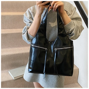 Détail du sac cabas noir brillant avec deux poches zippées frontales et pompons