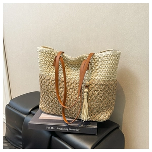 Detail of woven straw tote bag with mixed textures, fringe tassel and brown leather handle