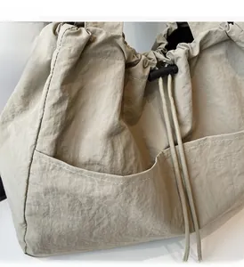 Detail view of large beige nylon tote featuring pleated texture and adjustable side drawstring