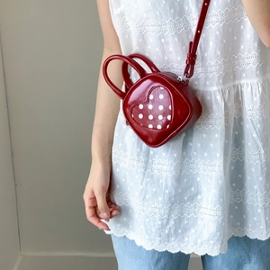 Detail of red heart-shaped mini bag with polka dot patch and adjustable strap on model