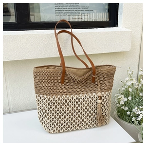 Detail of woven straw tote bag featuring two-tone texture with tassel and zipper closure