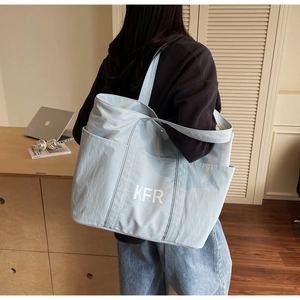 Close-up of light blue canvas tote bag with KFR logo and dual front pocket detail