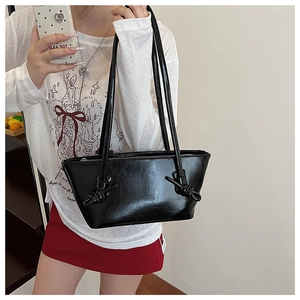 Détail d'un sac cabas noir brillant avec poignée à nœud et fermeture éclair sur un modèle