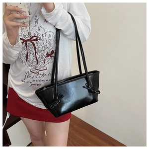Détail d'un sac d'épaule en cuir verni brillant noir avec nœud décoratif et fermeture éclair argent