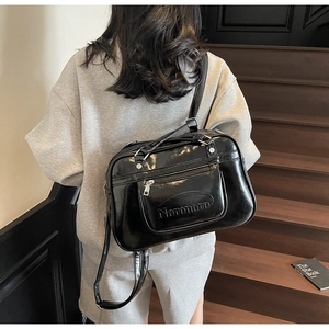 Detail of black glossy shoulder bag with embossed logo and adjustable strap on a staircase
