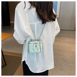 Detail of mint green quilted mini box bag with silver chain and metal flower charm