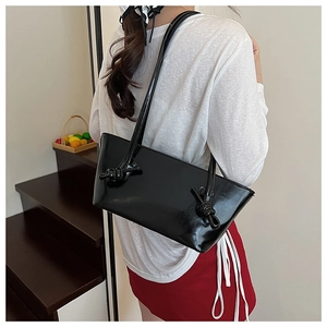 Détail du sac à bandoulière en cuir verni noir avec un design de nœud sur la sangle