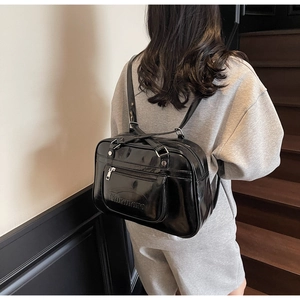 Detailed view of black patent leather backpack with polished finish and front zipper pocket