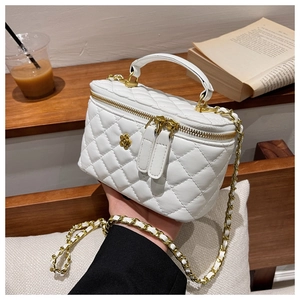 Detalle de un bolso cubo acolchado blanco con cadena dorada y un colgante de camelia