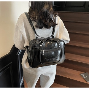 Detail of glossy black leather backpack showing the front pocket and embossed brand logo