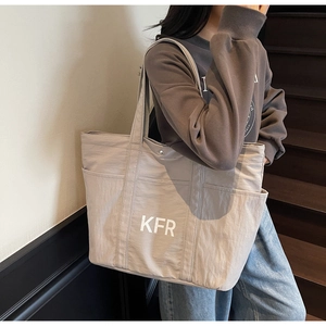 Detail of the side pocket on a beige canvas tote bag with KFR lettering and shoulder strap