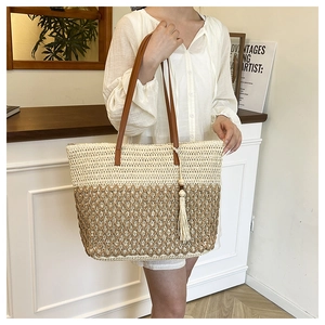 Detail of two-tone woven straw tote bag with leather straps and beaded tassel accent