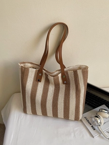 Chic striped straw tote bag with brown leather handles on a minimalist desk setting