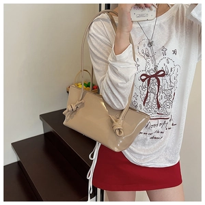 Gros plan du sac cabas en cuir verni beige avec détail de nœud sur la bandoulière