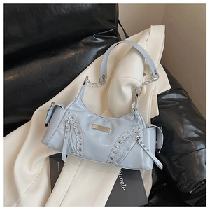 Détail du sac en cuir verni bleu clair avec clous argentés et fermetures éclair sur canapé