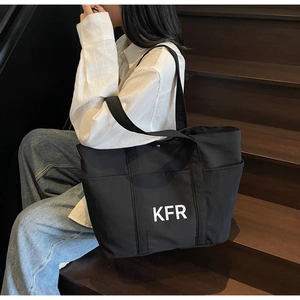 Close-up of a large black canvas tote bag featuring a white KFR logo on dark wooden stairs