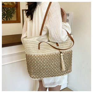 Detail of two-tone woven straw tote bag with brown leather straps and a stylish tassel