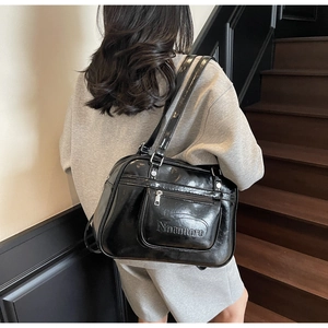 Close-up of a glossy black shoulder tote bag with zipper pocket on a wooden staircase