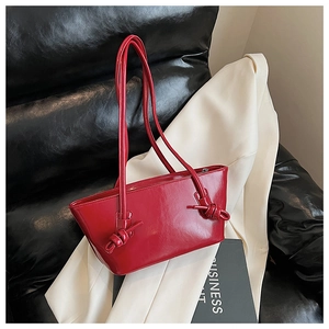 Détail du cabas en cuir verni rouge avec poignée à nœud posé sur un blazer blanc