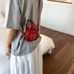 Close-up of a mini heart-shaped red crossbody bag with white polka dot detail in use