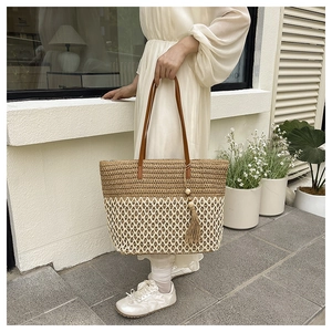 Detail of two-tone woven tote bag with leather handles and tassel charm for beach