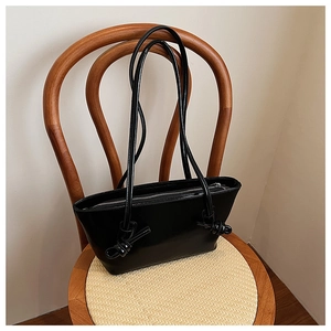 Détail du sac à main en cuir verni noir avec bandoulière nouée sur chaise vintage
