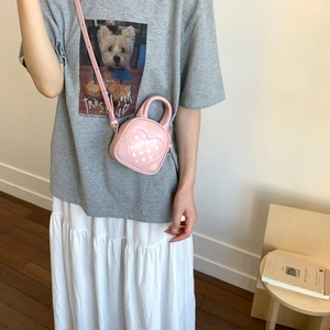 Pink heart-shaped PU mini crossbody bag with white polka dots shown on a female model
