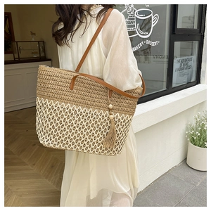 Detail of a large woven tote bag featuring bicolor stitching and leather straps with tassels