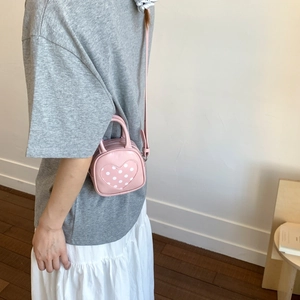 Detail of pink heart-shaped PU crossbody bag with white polka dot patch and slim strap