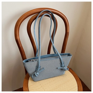 Détail du cabas en toile bleu clair avec bandoulières en cuir et décoration nouée