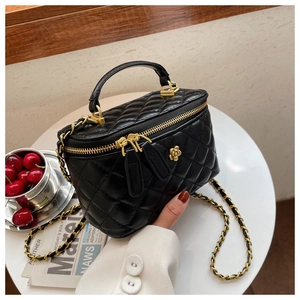 Detalle de bolso tipo cubo acolchado negro con cadena dorada y logo floral en mesa blanca