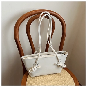 Détail du sac cabas en cuir crème avec bandoulière nouée posé sur une chaise en bois