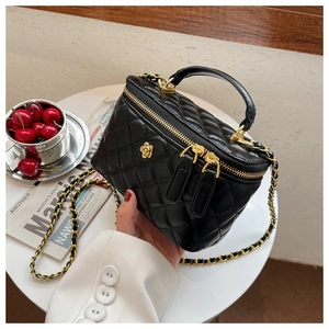 Detalle de mini bolso de cubo negro acolchado con cadena dorada y adorno floral